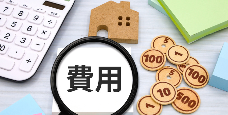 家のパネルとおもちゃのお金が置かれており、費用と書かれた紙を虫眼鏡で覗いている
