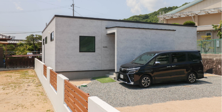 砂利が敷き詰められた広い駐車場が特徴のシンプルモダンな家の外観
