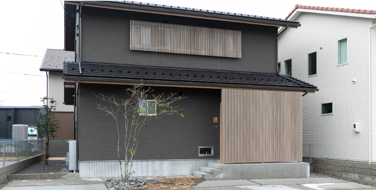 黒い外壁と玄関前の木が特徴的な家の外観