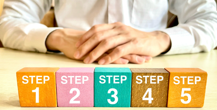 5つのSTEPが描かれたカラフルなキューブが机に置かれており、人が両手を添えて座っている