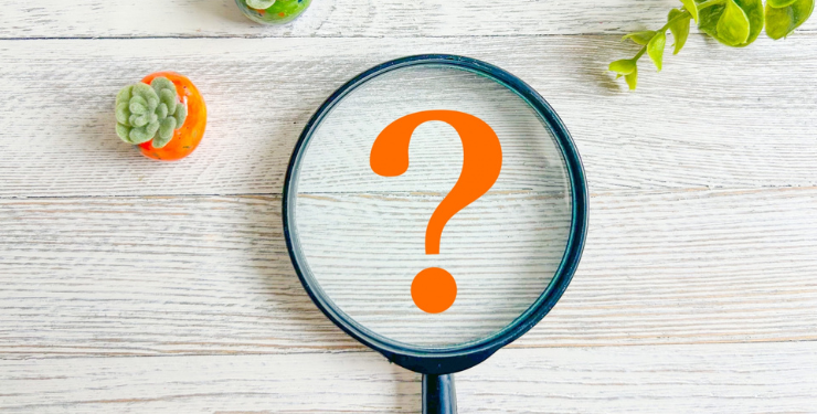 机に置かれたルーペの中にオレンジ色のクエスチョンマークが描かれている