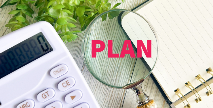 虫眼鏡にPLANと書かれており、電卓とノートが置かれている