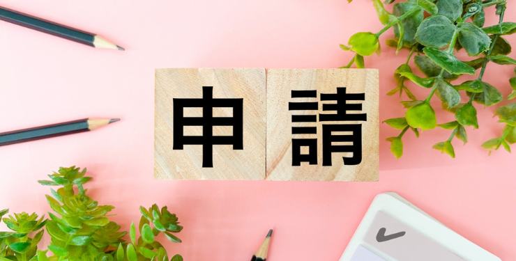 ピンクの背景に、申請と書かれた木製キューブが置かれている