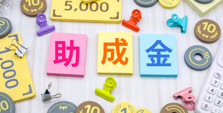 助成金と書かれたパネルの周りに小お金のおもちゃが並んである