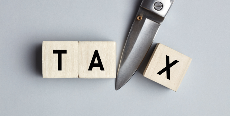 TAXと書かれた木のキューブのTAとXの間をハサミで切って、減税を表している