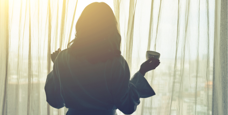 朝日の差し込む部屋で外を見る女性