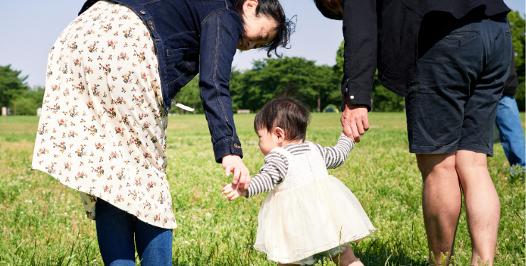 公園で、子供の両手を両親が両側から繋いでいる様子