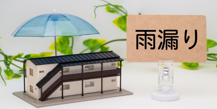 マンションの模型の上に傘がさしてあり、雨漏りという看板が置かれている
