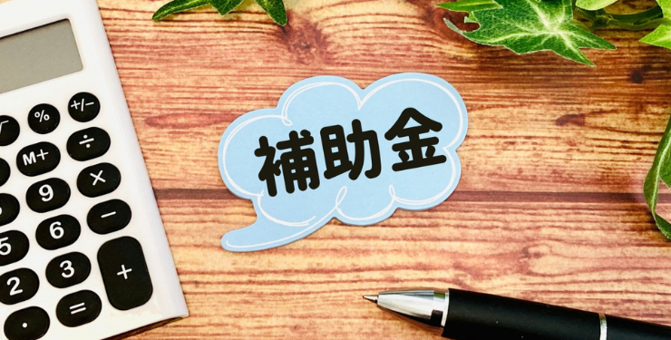 補助金と書かれた吹き出し型のメモの周りに電卓とボールペンが置かれている