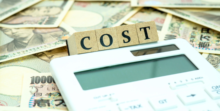 大量の一万円の上に電卓とCOSTと書かれたブロックが置かれている
