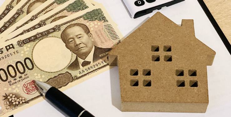 家の形の木製と一万円札と電卓とボールペンが紙の上に置かれている