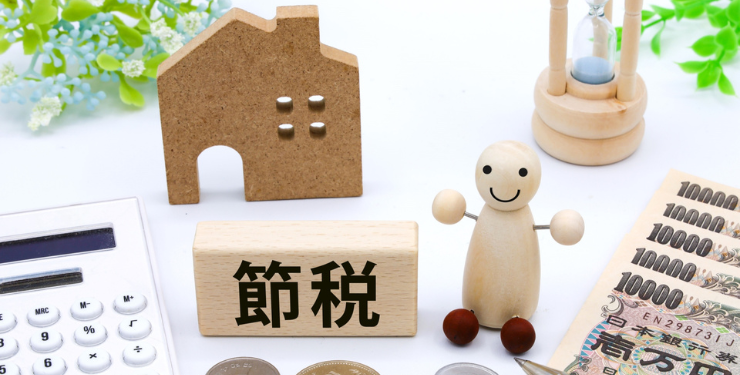 節税と書かれたブロックの周りに、家の模型と人形と一万円札と電卓が置かれている