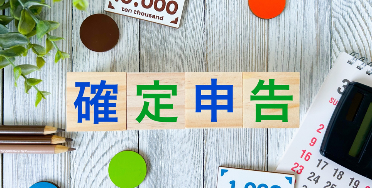 確定申告と書かれたブロックの周りにカラフルなお金のおもちゃが置かれている