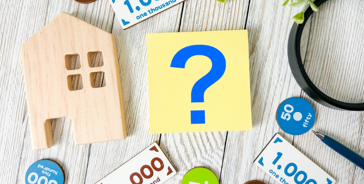 家のパネルとお金のおもちゃ、大きなクエスチョンマークが机の上にある