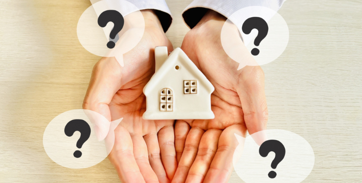 家の模型を両手で支えており、周りにクエスチョンマークが有る